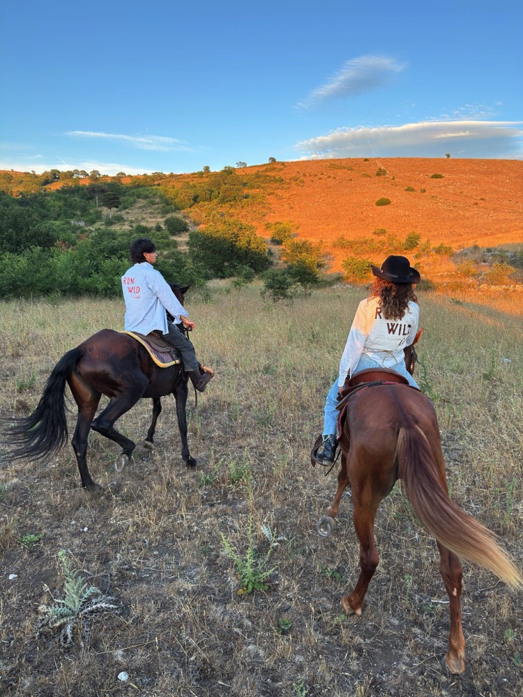 Coppia a cavallo al tramonto nella valle con maglie Run Wild